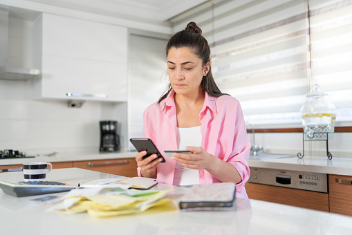 Woman Paying Taxes With Credit Card On Smartphone Banking On Kitchen