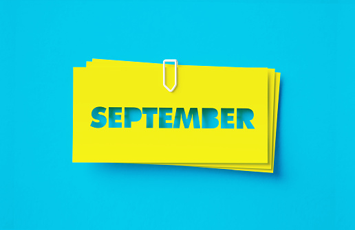 September written cut out yellow adhesive notes sitting on blue background. Horizontal composition with copy space.