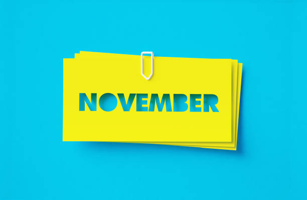 November written cut out yellow adhesive notes sitting on blue background. Horizontal composition with copy space.