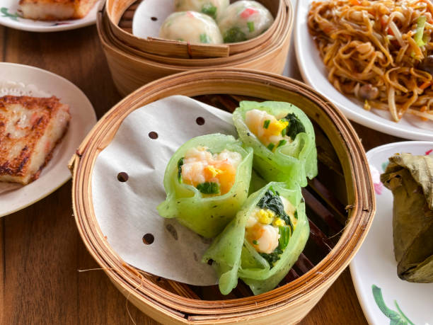 spinach shrimp dumplings dim sum in a bamboo steamer on a table. pan-fried carrot cake, crystal chives dumplings, and noodles in the background. - crystal noodles imagens e fotografias de stock