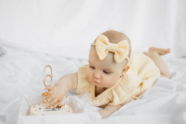 istock Happy baby with yellow bow on head lying on bed with white background. 1408208535