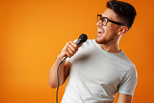 Hispanic young handsome man singing with joy in microphone clsoe up