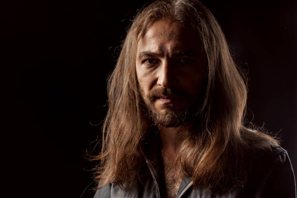 Long-haired masculine middle-aged man standing in the dark close up