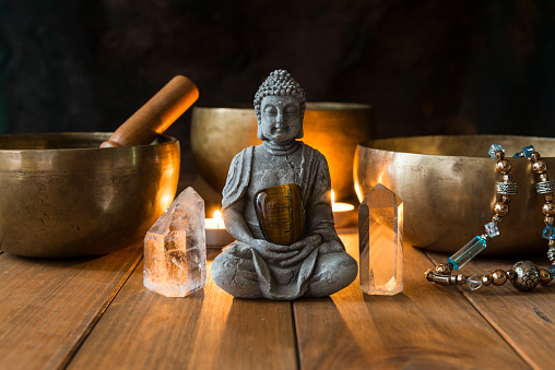 Still life with singing bowls, minerals, candles and a Buddha figure on wooden boards and a dark background. Small altar illuminated with small candles for meditation and music therapy.