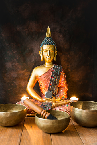 Still life with Tibetan bowls, minerals, candles and a Buddha figure on wooden boards and a dark background. Small altar illuminated with small candles for meditation and music therapy.