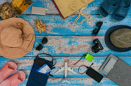 Man and woman vacation accessories on the blue wooden boards. Travel hats, camera, glasses, ticket holder, flip-flops, reader, magazine, plane figure.. Top view. Place for text or logo in center.