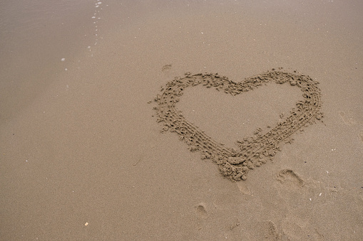 A woman is drawing Heart shape on beach sand. A hand drawn love sign on the beach