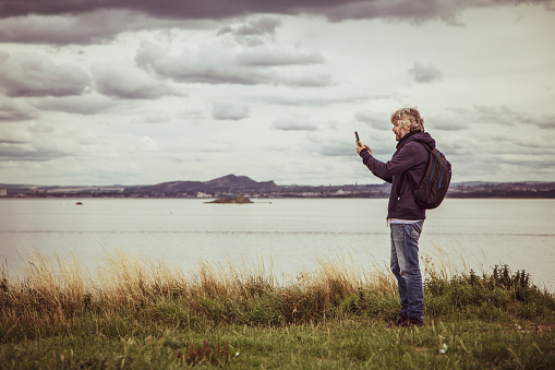 man takes pictures with his mobile phone in nature in a cloudy sky with copy space