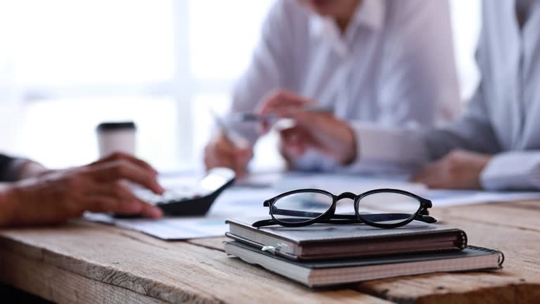 Focusing on the glasses, behind the scenes a group of businessmen are meeting with staff in the marketing department, planning and brainstorming meetings to grow the company.