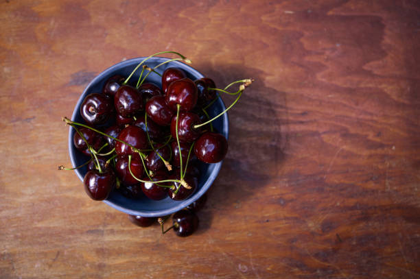 istock Flat lay. Fresh ripe purple cherry berries in blue ceramic bowl on rustic wooden table. Still life, copy space for text 1408219155