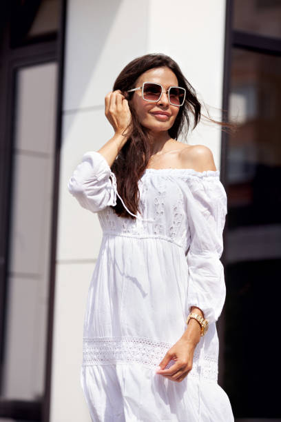 splendida donna bruna in vestito di cotone bianco e occhiali da sole all'aperto - long long hair dress young adult foto e immagini stock