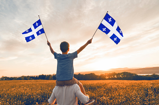 A Patriotic father and child waving Quebec flags on sunset