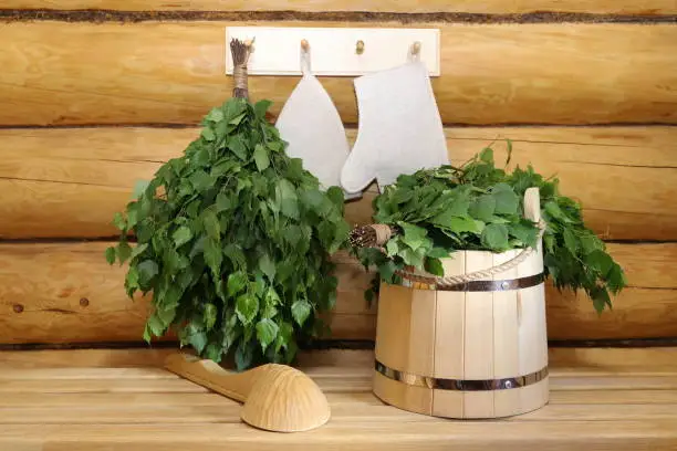 A fresh birch broom and traditional sauna accessories on a wooden bench  and on a hanger on a log wall.