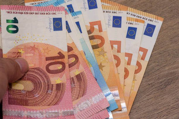 Man holding euro coin Man holding euro coins on wooden table para birimi stock pictures, royalty-free photos & images