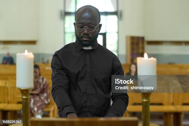 Priest Standing By Pulpit Between Two Burning Candles During Church Service Stock Photo - Download Image Now