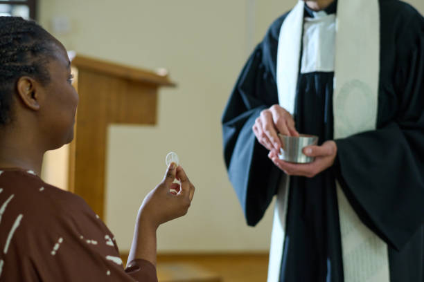 Young black woman holding unleavened bread symbolizing flesh of Jesus Christ while taking communion during liturgy in Catholic church