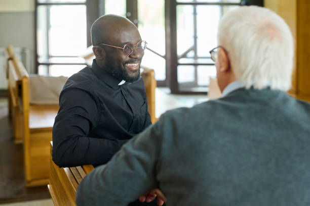 Happy young African American pastor of evangelical church consulting aged man Young cheerful African American pastor of evangelical church consulting aged grey haired male parishioner after sermon religious occupation stock pictures, royalty-free photos & images