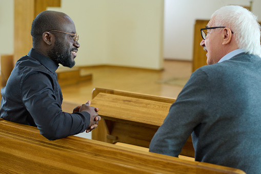 Young African American pastor consulting senior male parishioner in church