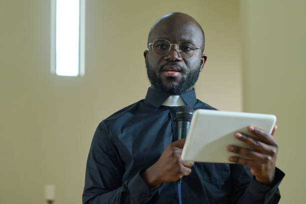 istock Young confident black man with microphone and digital tablet making speech 1408224375
