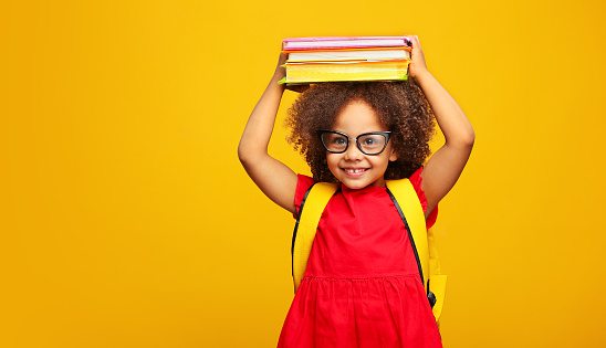 divertida niña negra sonriente de la escuela con gafas sostiene libros en su cabeza photo