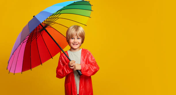 istock Cheerful child boy in red raincoat under a colored umbrella on colored yellow background. Copy space 1408225737