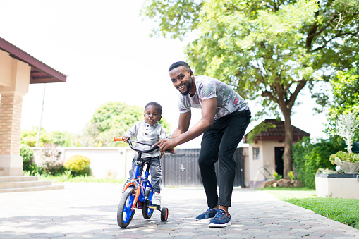 Young father helps toddler ride tricycle