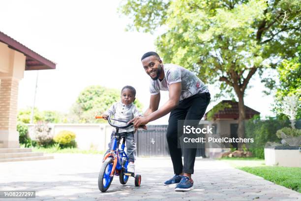 Young Father Helps Toddler Ride Tricycle In Driveway Of Home Stock Photo - Download Image Now