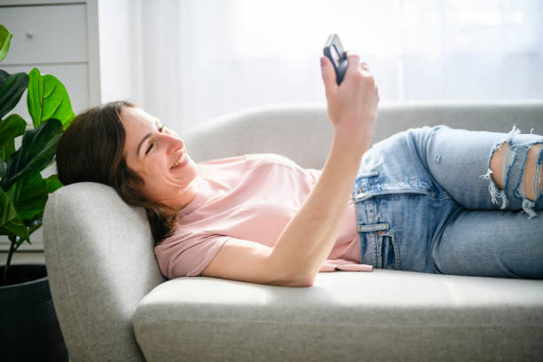 istock friendly looking long-haired girl using cellphone sitting at home on couch 1408227343