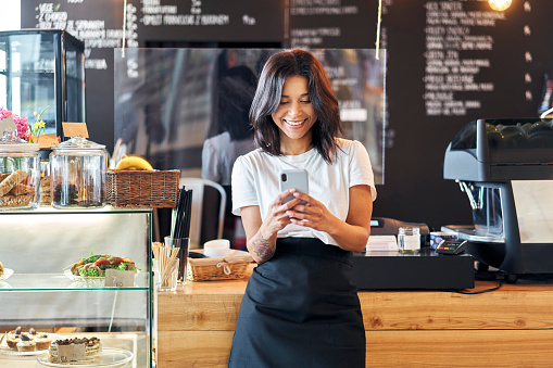 Retrato de una camarera barista sonriente usando el teléfono móvil en el trabajo photo