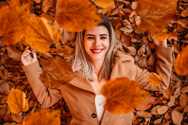 Beautiful young woman lying on autumn leaves in park and smiling.