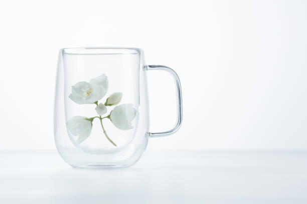 White jasmine flowers in a glass cup on a white background with copy space, close up. Shallow depth of field