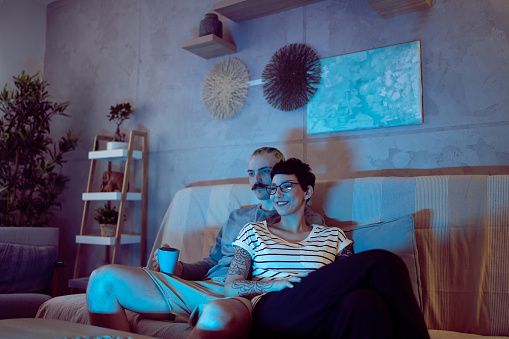 Modern young Caucasian couple sitting on the sofa while watching movie on TV