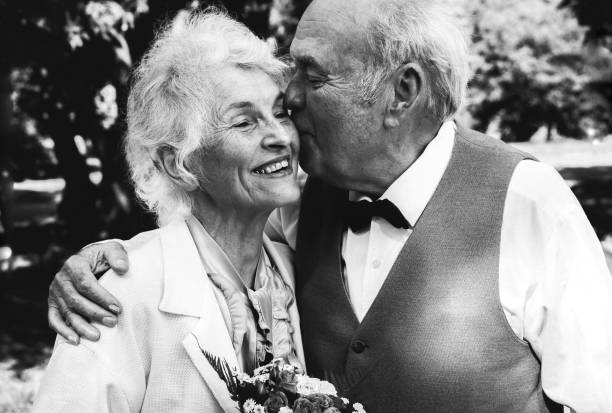 老夫婦が緑の公園を歩いている。彼らの黄金の結婚記念日のお祝いで祖母と祖父。50年一緒にラブストーリー。おばあちゃんとおじいちゃんがキスをする。白黒。 - white black portrait women ストックフォトと画像