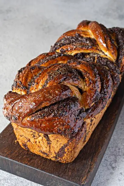 Freshly baked brioche/Babka with poppy seeds and chocolate on a wooden board. Braided dessert bread. Homemade baking, national pastries. Estonian kringle in the shape of a brick.