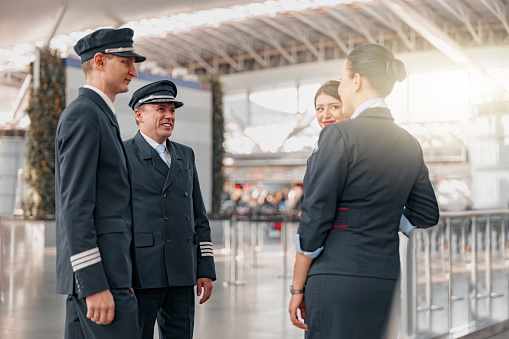 Smiling plane team in uniform standing and talking in airport terminal