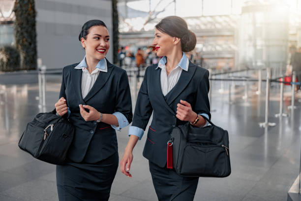 Smiling pretty flight attendants with bags talking in the terminal stock photo