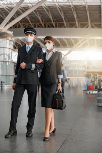 stewardess and pilot in protective face masks walking in the terminal - cabin crew pilot airport walking imagens e fotografias de stock