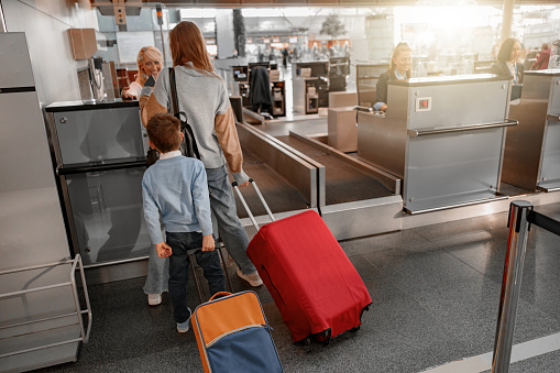 Back view of mother and his son holding suitcases and going through passport control in the airport