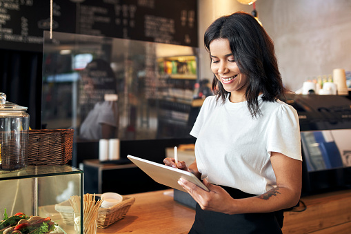 Happy waitress barista using digital tablet at work in cafe, restaurant