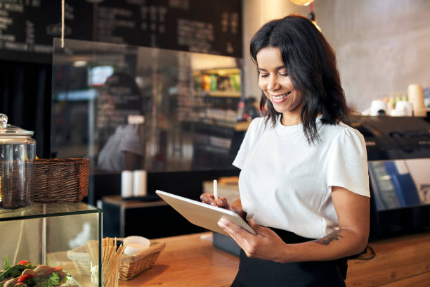 Happy waitress barista using digital tablet at work in cafe, restaurant stock photo