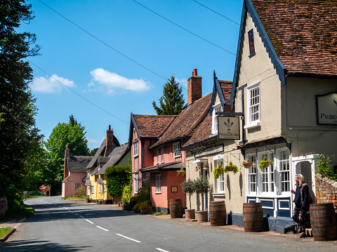 A main street in the pretty village of Chelsworth in Suffolk, Eastern England, where a woman is leaving the Peacock Inn, an old public house.