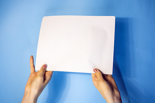 hand holding white blank paper isolated on blue background with clipping path.Holding a sign that says Covid 19