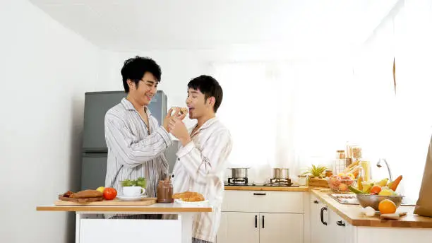 Photo of Happy gay couple enjoy breakfast in kitchen drinking coffee. Two best friends LGBTQ relation partner home cooking. Happiness romance homosexual marriage lifestyle. Two men together love friendship.