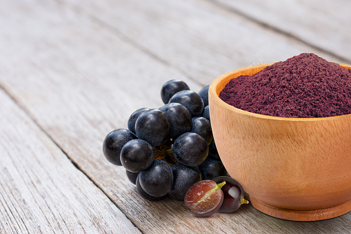 Grape extract flour (opc grape powder) in wooden bowl and fresh black grapes isolated on wooden table background. Copy space.