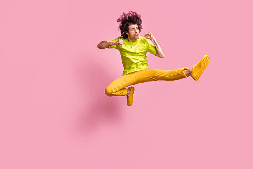 Full size photo of impressed guy jumping karate look empty space wear t-shirt trousers sneakers isolated on pastel pink background.