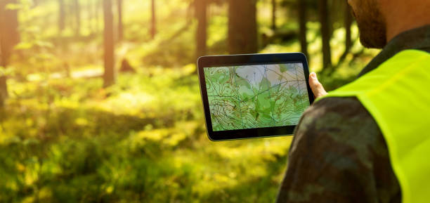 man working with topographic map data on digital tablet in forest. banner with copy space - geografia física imagens e fotografias de stock