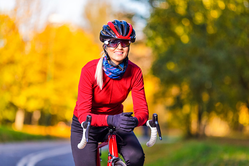Ideas de ciclismo de carretera. Ciclista femenina encantadora con un atuendo cálido posando en bicicleta de carretera mientras sonríe y se prepara para comenzar al aire libre en el contexto otoñal. photo