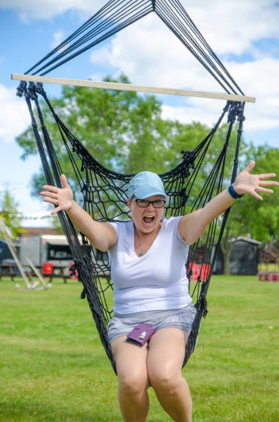 Mature woman in hammock chair Mature woman in hammock chair in public park during summer day woman wearing baseball cap stock pictures, royalty-free photos & images