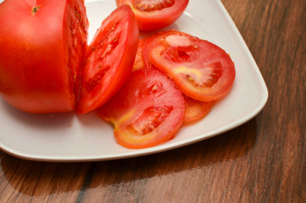 Sliced tomatoes inside a white plate on a wooden table with diagonal top view. Sliced tomatoes inside a white plate on a wooden table with diagonal top view. madeira sauce stock pictures, royalty-free photos & images