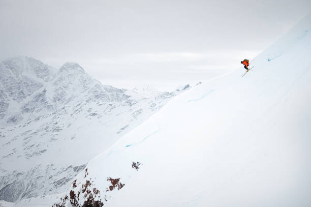 un joven esquía rápidamente por un glaciar cubierto de nieve con el telón de fondo de altas montañas - freeride fotografías e imágenes de stock